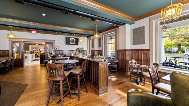 A spacious restaurant with wooden flooring, a central island with bar stools, and large windows offering a view of the outdoors. - The White Inn (Fredonia)