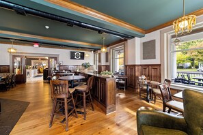 A spacious restaurant with wooden flooring, a central island with bar stools, and large windows offering a view of the outdoors. - The White Inn (Fredonia)