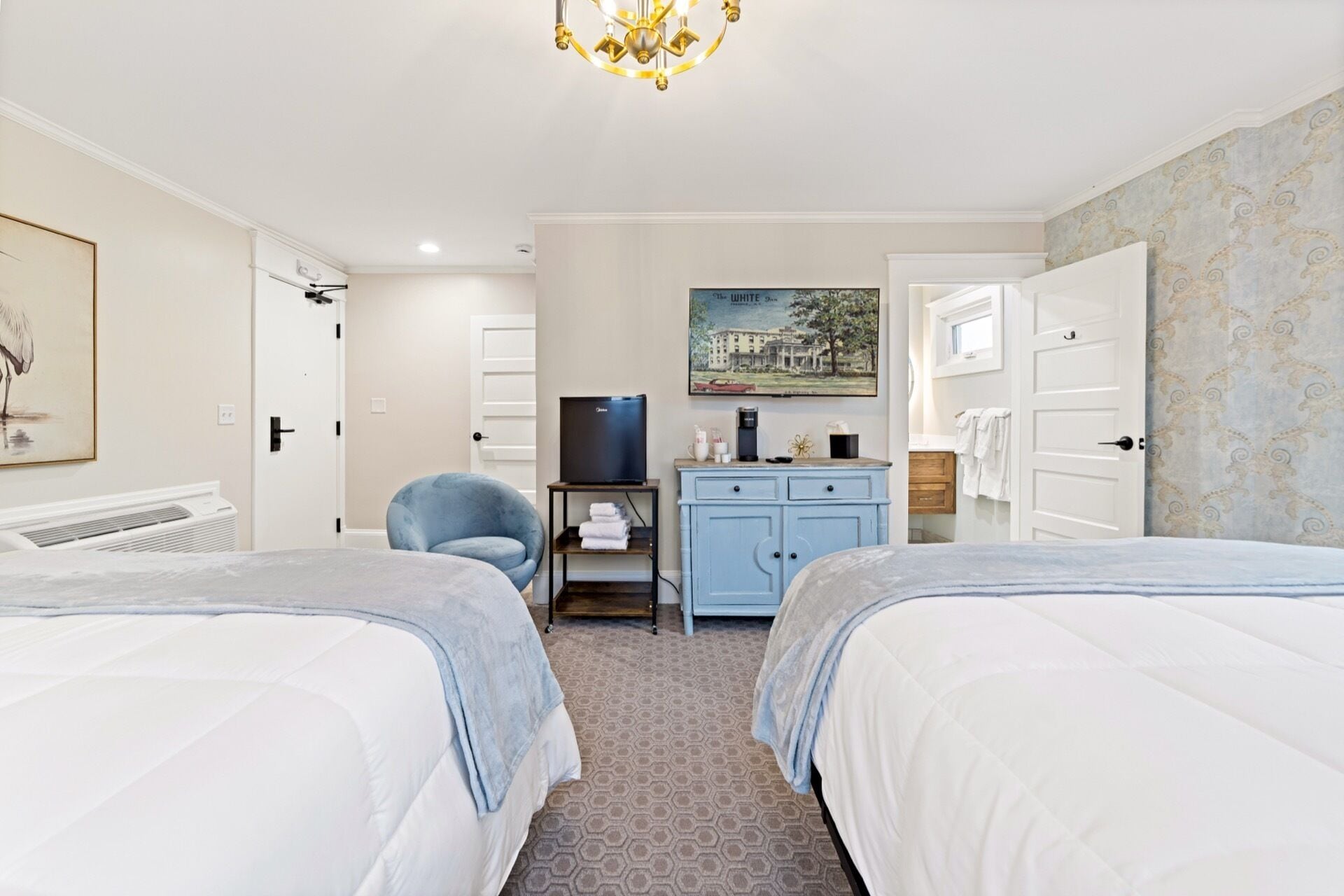 A hotel room with two beds, a desk with a television, a chair, and a painting on the wall.