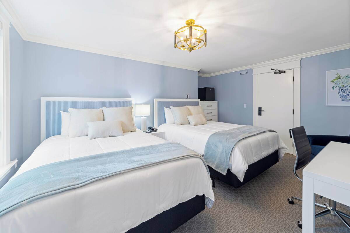 Ein Hotelzimmer mit zwei Betten, einem Schreibtisch, einem Stuhl, einer Chandelier und einer Tür.