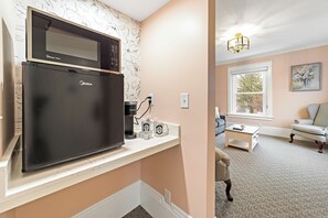 A kitchen with a black Midea refrigerator and a microwave, a coffee maker, and a countertop with mugs. There is a window with a view of trees and a painting on the wall.