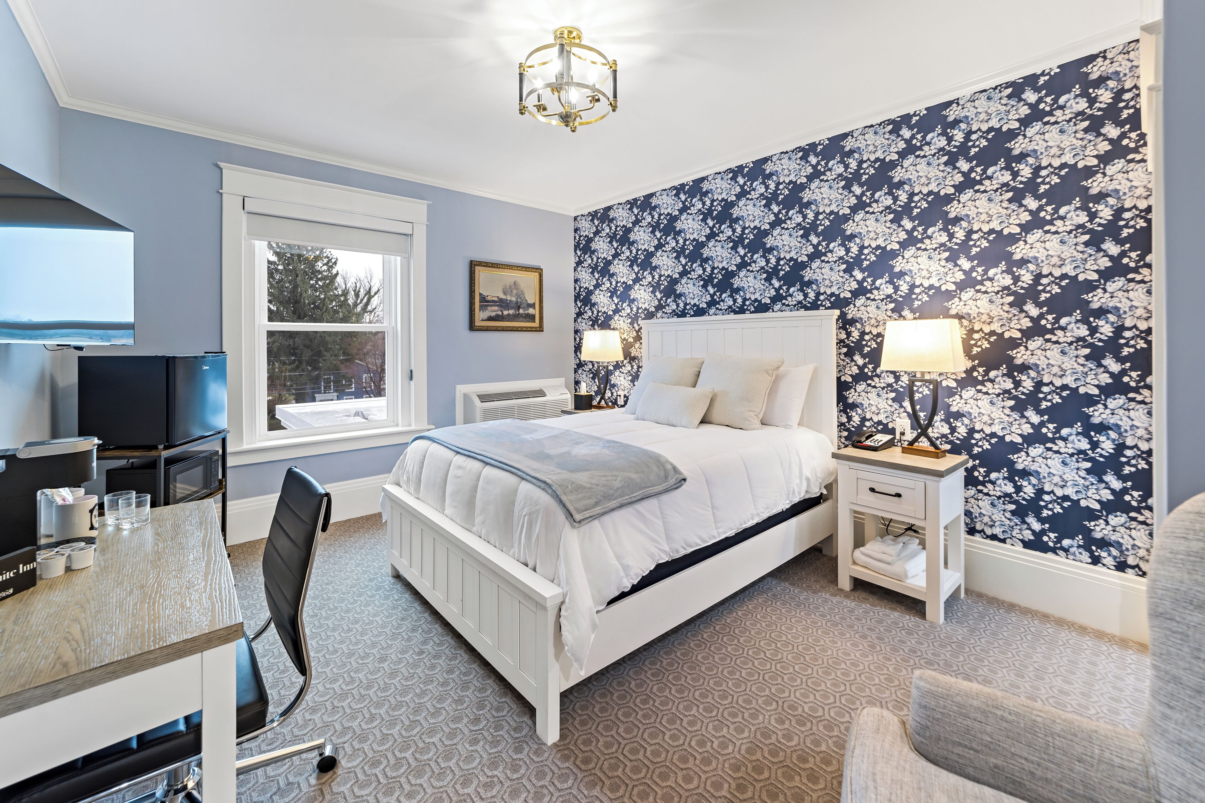 A hotel room with a bed, bedside tables, a desk with a chair, a television, and a window.