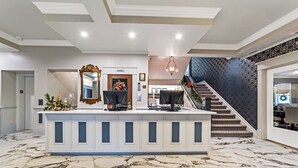 A reception area with a marble floor, a reception desk with a large mirror, and a staircase leading to a balcony. - The White Inn (Fredonia)