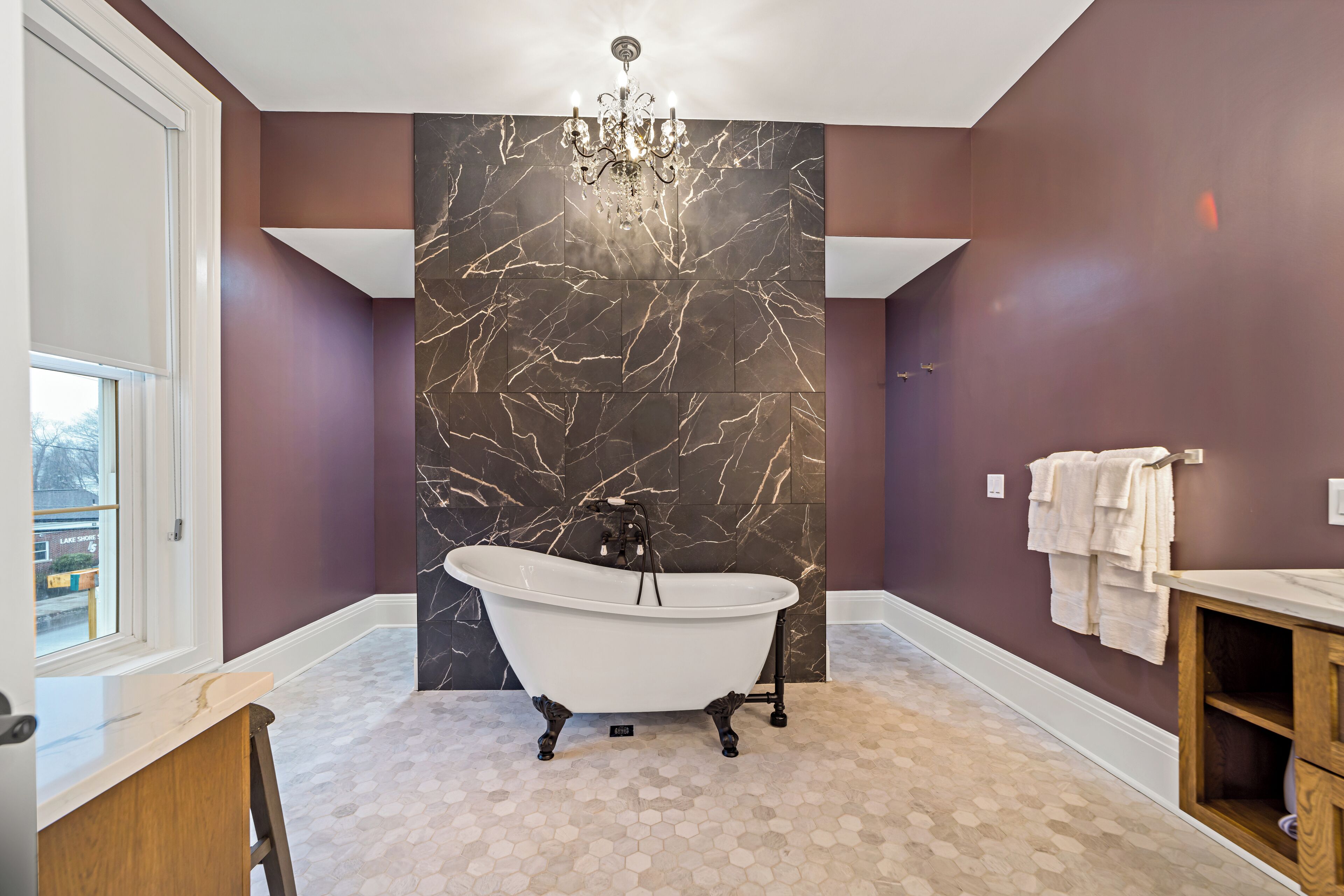 A bathroom with a freestanding bathtub, a chandelier, and a marble wall.