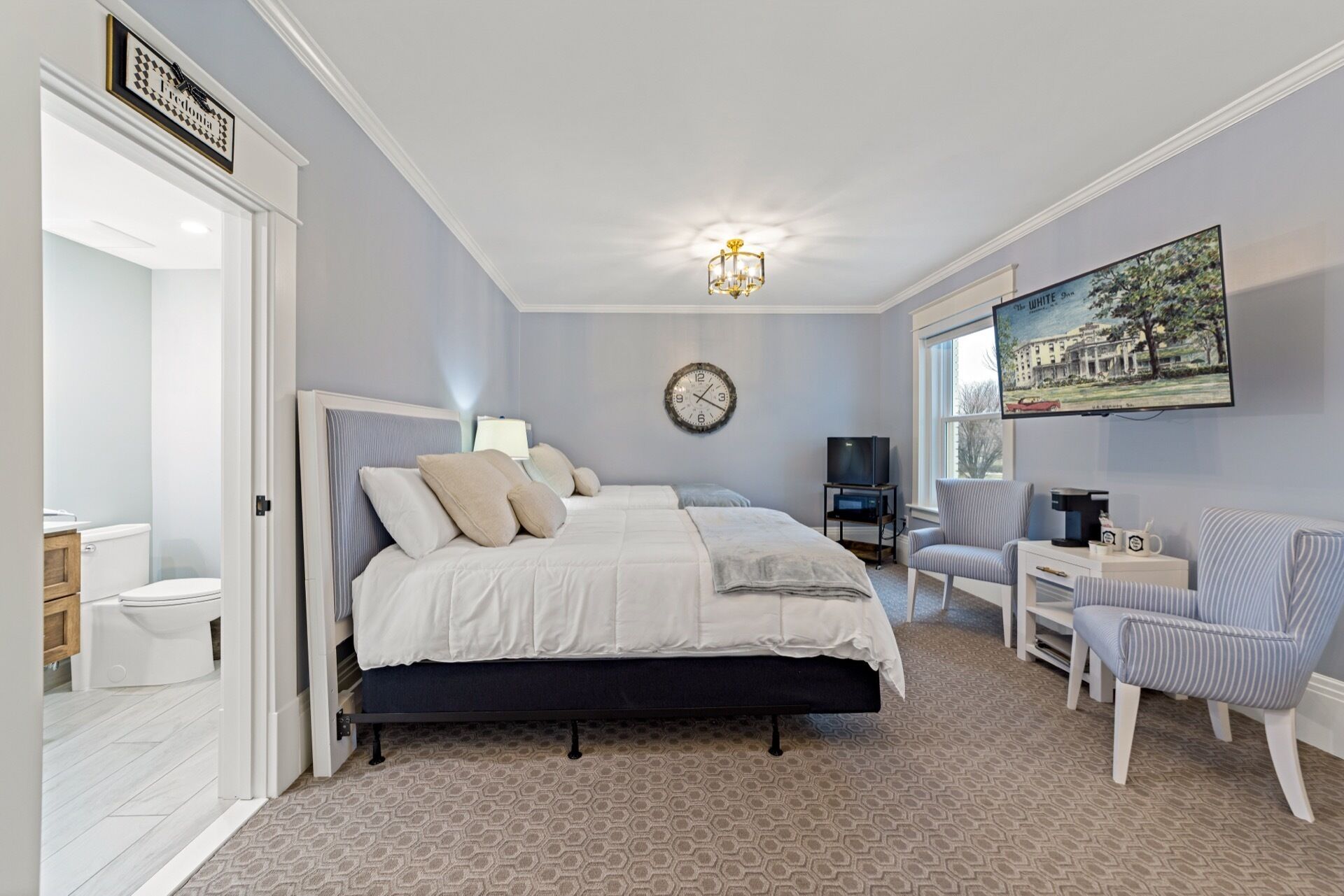 A bedroom with a bed, bedside table, chair, TV, and a painting on the wall.
