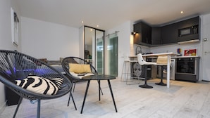 A modern kitchen with dark cabinets, a microwave, and a dishwasher. There is a dining area with a table and chairs, and a living area with a sofa and a chair. - Nice apartment in Sainte-Maxime with WiFi (Sainte-Maxime)