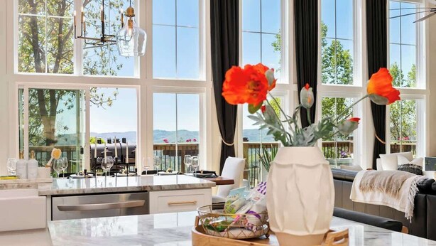 Eine moderne Küche mit Marmorarbeitsplatte, einer Blumenvase und Blick ins Freie durch große Fenster.