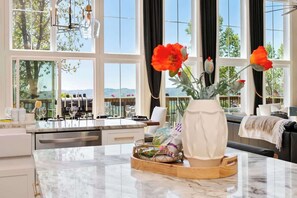 A modern kitchen with a marble countertop, a vase with flowers, and a view of the outdoors through large windows.