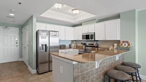 Una cocina moderna con armarios blancos, electrodomésticos de acero inoxidable, encimera de granito y una pequeña isla con taburetes.