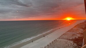 Una playa con un atardecer, el océano y algunas personas caminando.