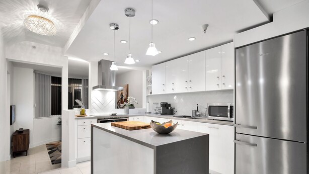 Une cuisine moderne avec des meubles blancs, des appareils en acier inoxydable et des luminaires suspendus.