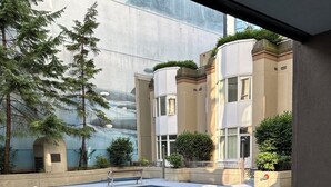 Un espace piscine intérieure paisible, avec un pont en pierre, entouré d’arbres et de bâtiments modernes.