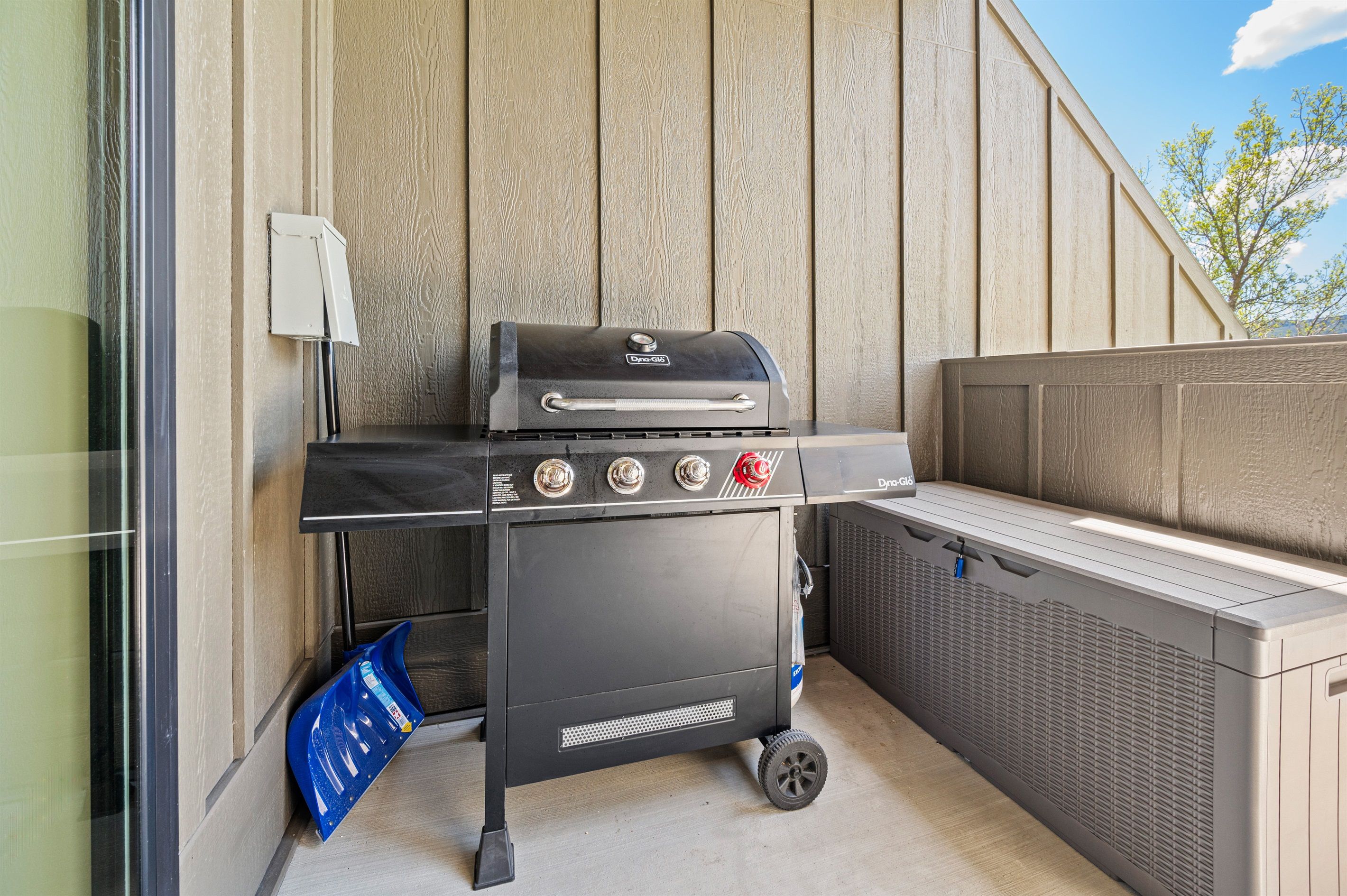 Una parrilla portátil con cuatro quemadores y un compartimento de almacenamiento lateral, frente a una pared de madera.