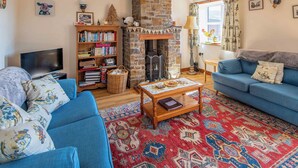 A cozy living room with a stone fireplace, a blue sofa, a bookshelf, and a television. - The Old Shippen - UK48328 (Lifton)