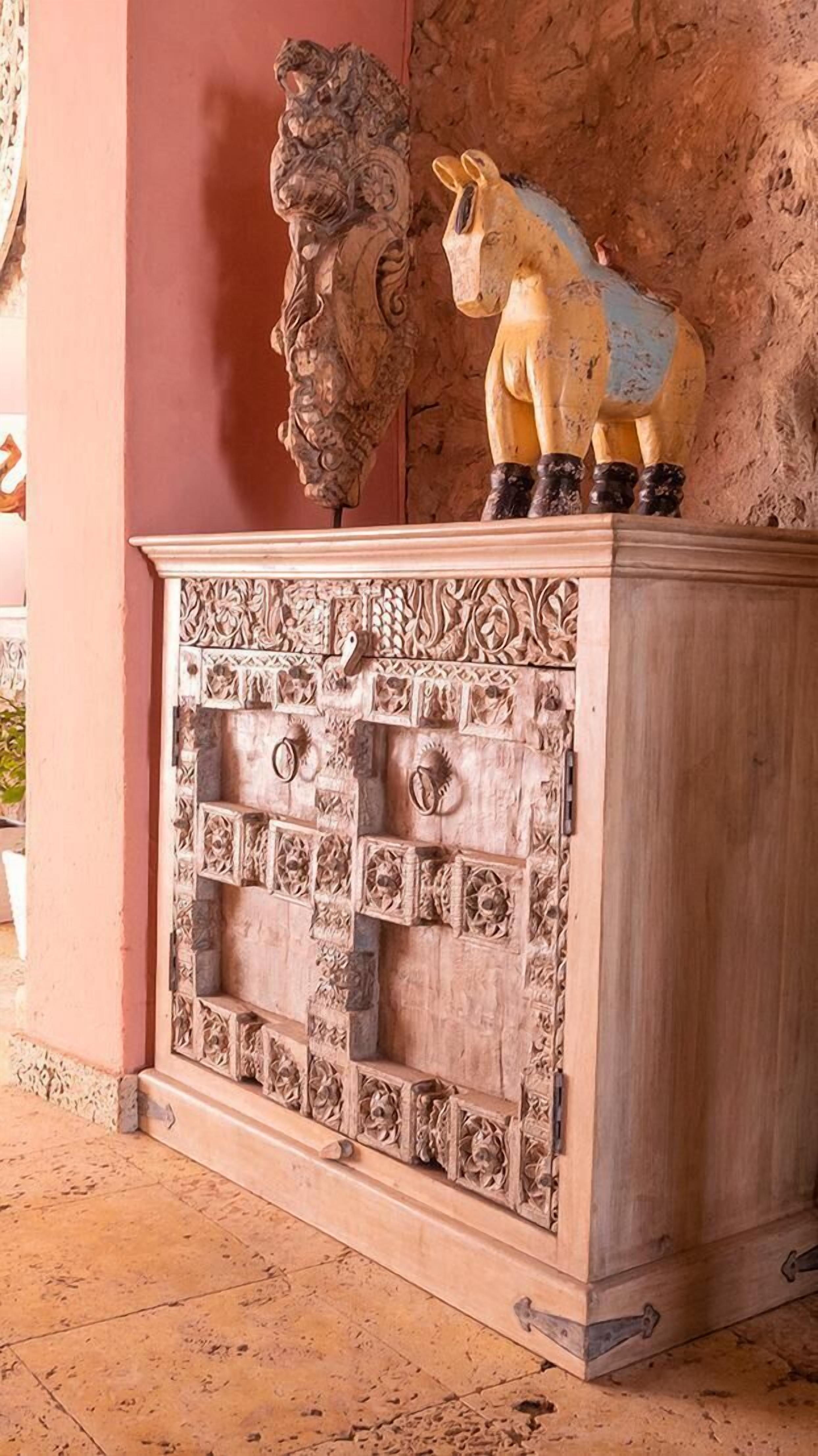 A carved wooden cabinet with intricate designs and a lion and horse sculpture on top.