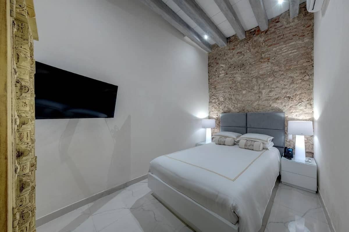 Quarto moderno com parede de destaque em pedra, uma cama grande, abajures e uma TV de tela plana fixada na parede.