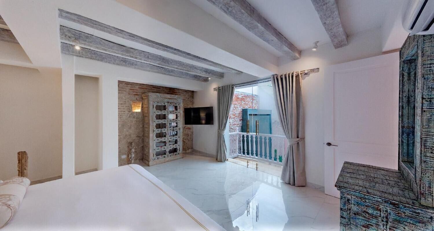 Un dormitorio moderno con una cama grande, televisión y balcón con cortinas.