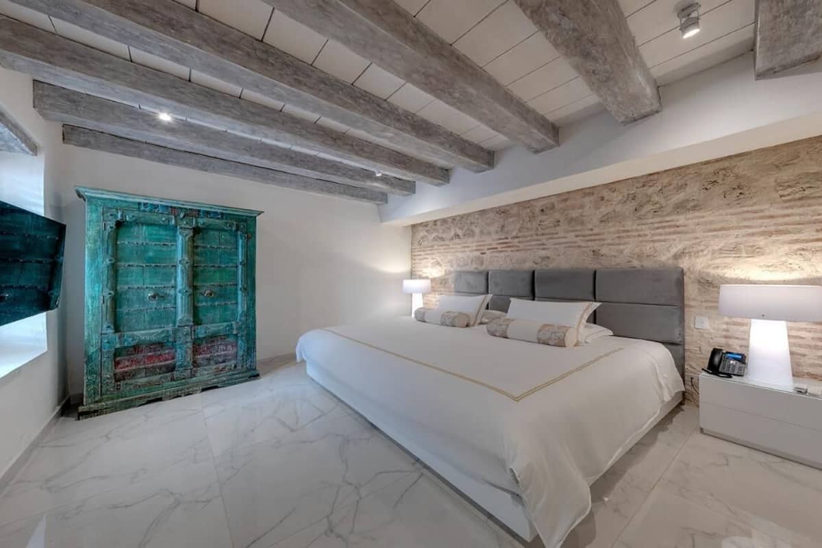 Quarto com uma cama grande, teto de madeira, parede de pedra e porta azul-turquesa.