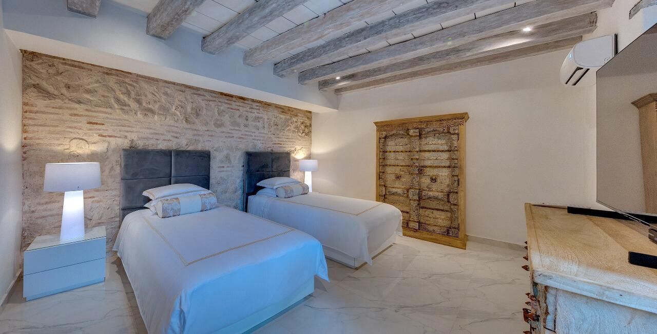 Ein Schlafzimmer mit zwei Betten, einer Steinwand, einer Holztür und einem kleinen Nachttisch mit Lampe.