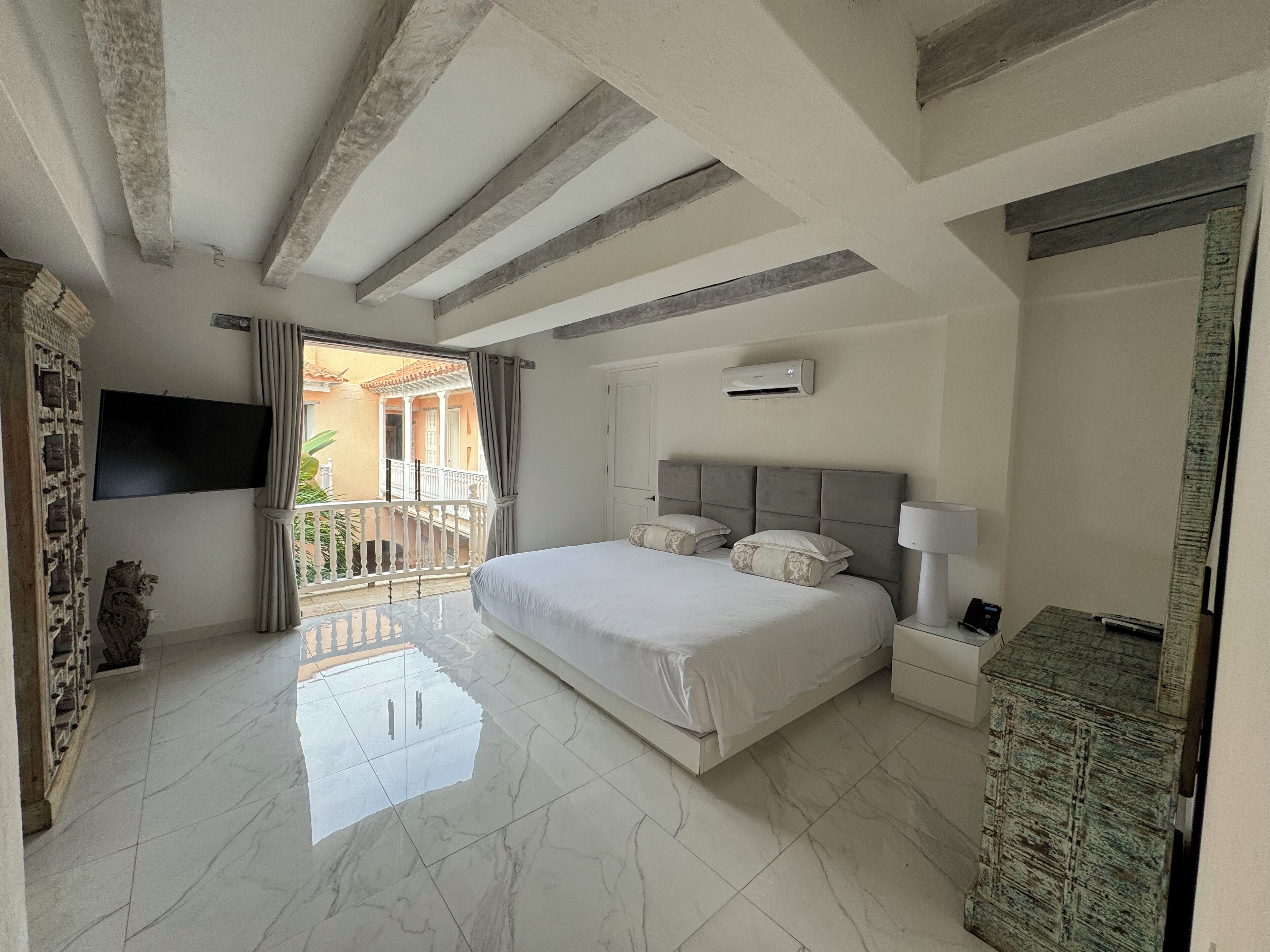 Un dormitorio con una cama grande, un televisor instalado en la pared y un balcón con vistas al exterior.