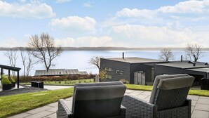 A modern outdoor seating area with wicker chairs, a patio, and a view of a lake and distant shoreline.