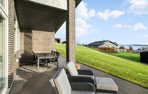 Relax in a serene outdoor space with a dining table, chairs, and comfortable sofas, surrounded by a patio and lawn.