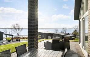 Relax on the patio with a view of the calm lake, surrounded by a well-maintained lawn and a pathway to a covered structure.