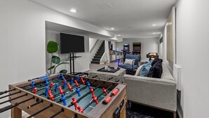 Ein modernes Wohnzimmer mit Fußballtisch, einer Couch, einem Fernseher und einer Treppe zu einer weiteren Ebene.
