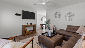 Ein modernes Wohnzimmer mit einem braunen Ledersofa, einem Holztisch und einem an der Wand befestigten Flachbildfernseher.