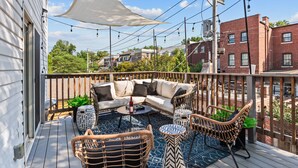 Una terraza con sofá, sillas y una mesa, con vistas a un barrio residencial.