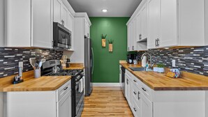 Una cocina moderna con armarios blancos, encimera de madera, pared de acento verde y salpicadero de azulejos.
