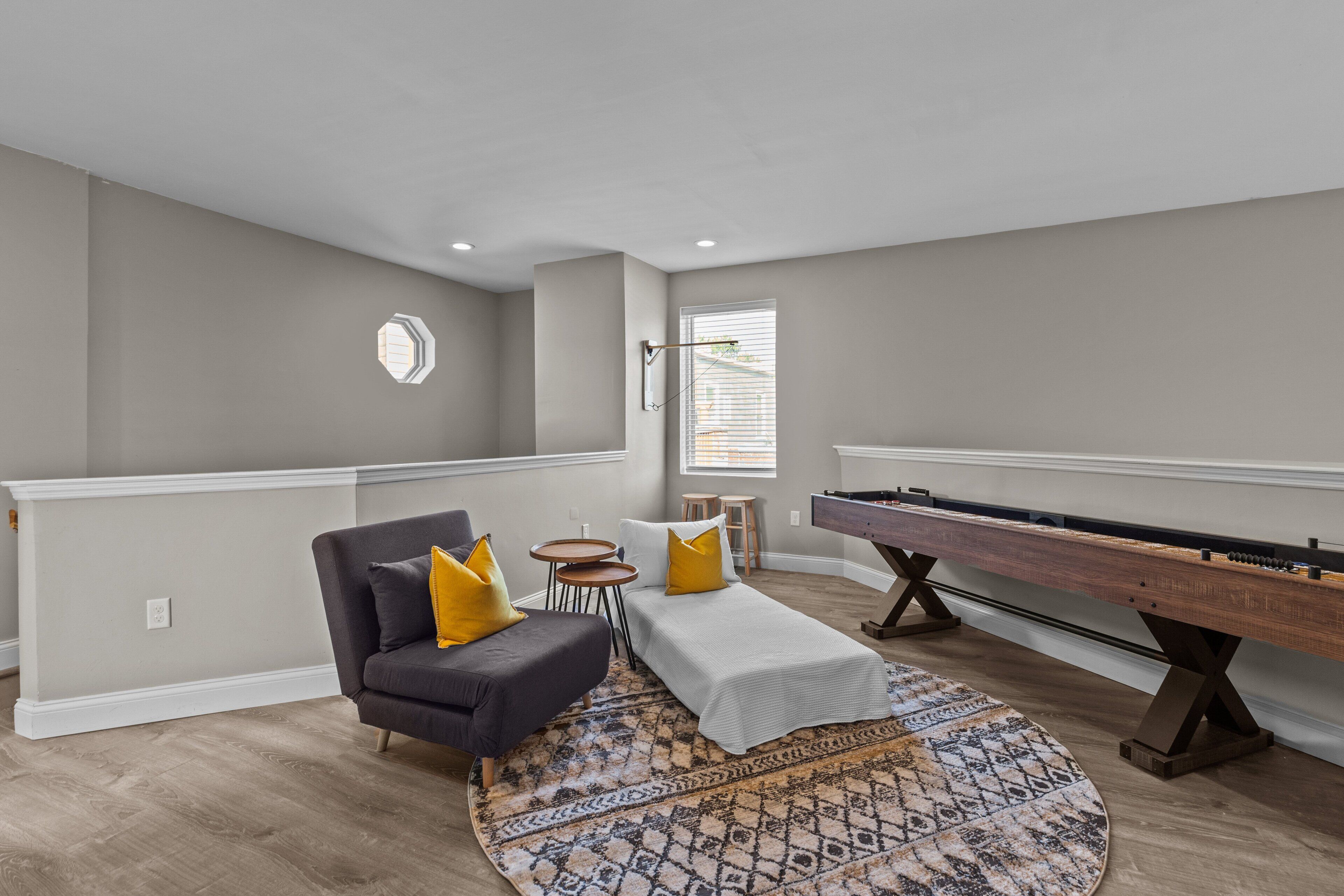 A living room with a dark sofa, a small round table, a bed, a pool table, and a patterned rug.