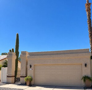 Un garage d’habitation avec un ciel dégagé, un grand cactus et une plante en pot.