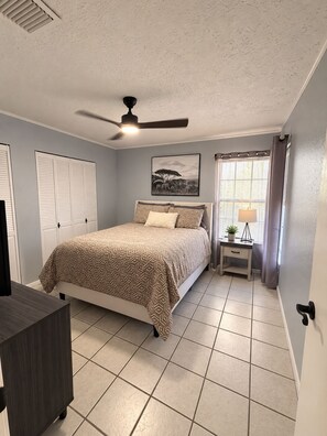 A bedroom with a bed, a ceiling fan, a window with curtains, and a bedside table with a lamp.