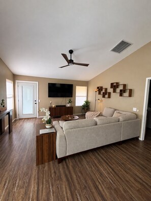 A living room with a sofa, a coffee table, a TV, a ceiling fan, and a door.