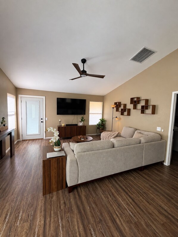 Un salon avec un canapé, une table basse, un téléviseur, un ventilateur de plafond et une porte.