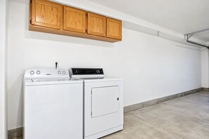 A laundry room with a white washer and dryer, wooden cabinets above, and a concrete floor.