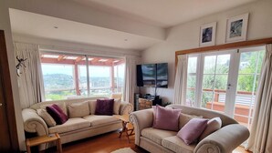 Sala de estar com dois sofás, televisão e vista para o exterior.
