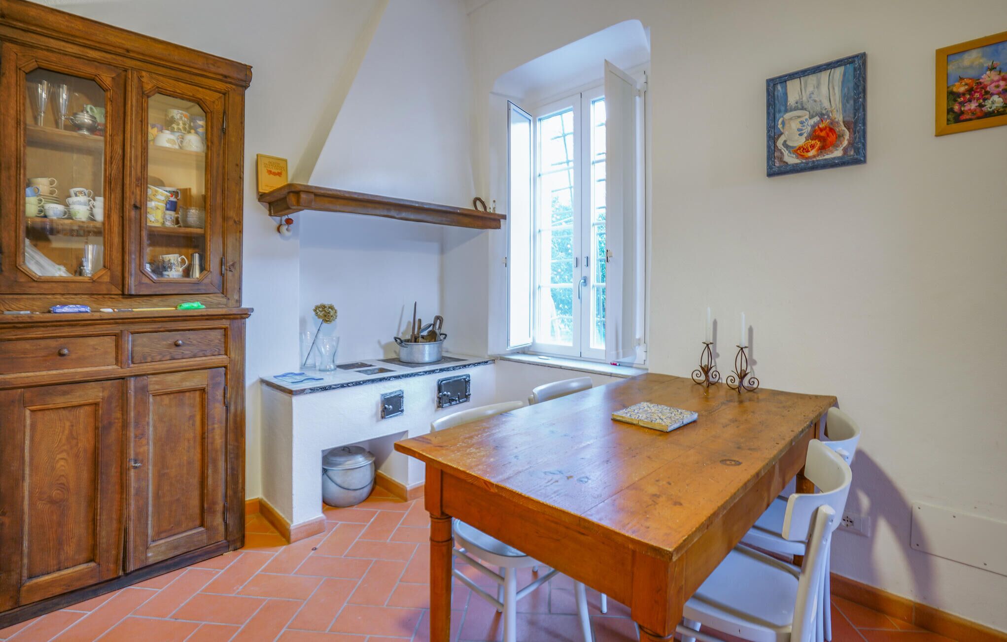 Una cucina con un tavolo di legno, sedie bianche, un fornello e una finestra.