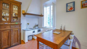 Una cucina con un tavolo di legno, sedie bianche, un fornello e una finestra.