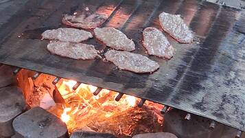A grill over an open fire pit with meat being cooked.