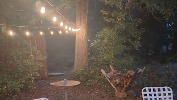 Un espace extérieur aménagé avec deux chaises en métal blanc, une petite table ronde et une guirlande lumineuse.