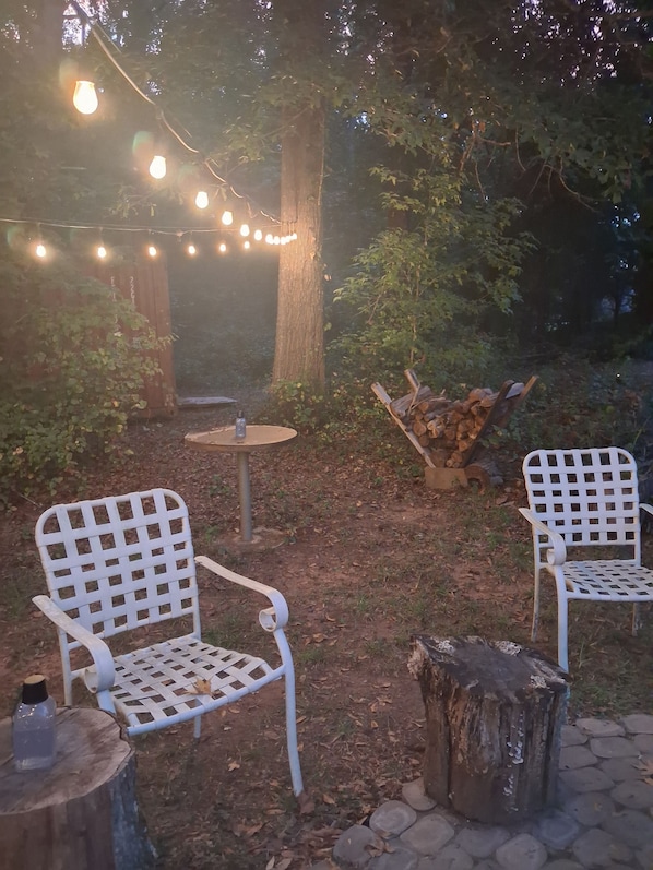 An outdoor seating area with two white metal chairs, a small round table, and a string of lights.