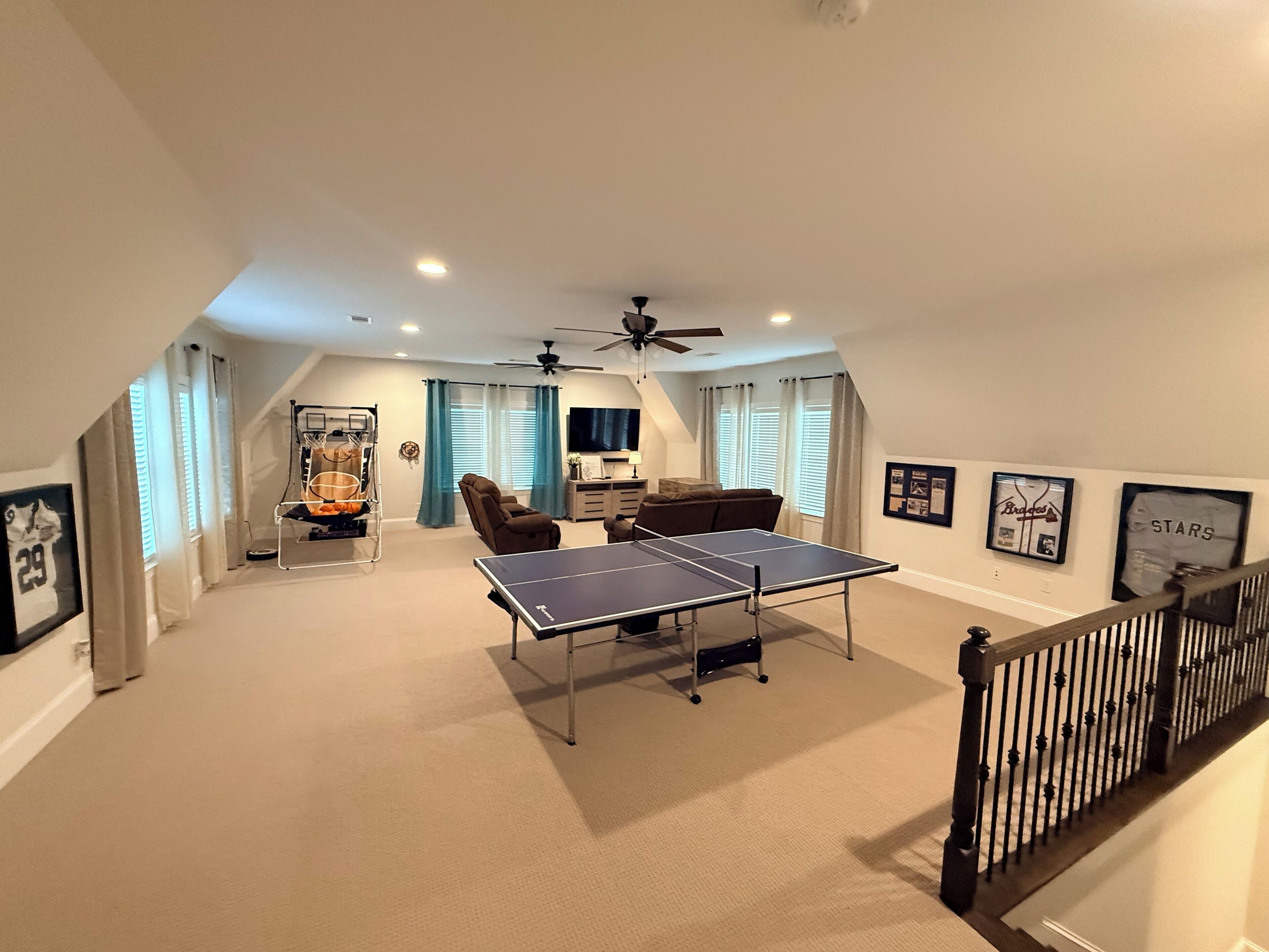 A spacious room with a ping pong table, ceiling fans, and a staircase.