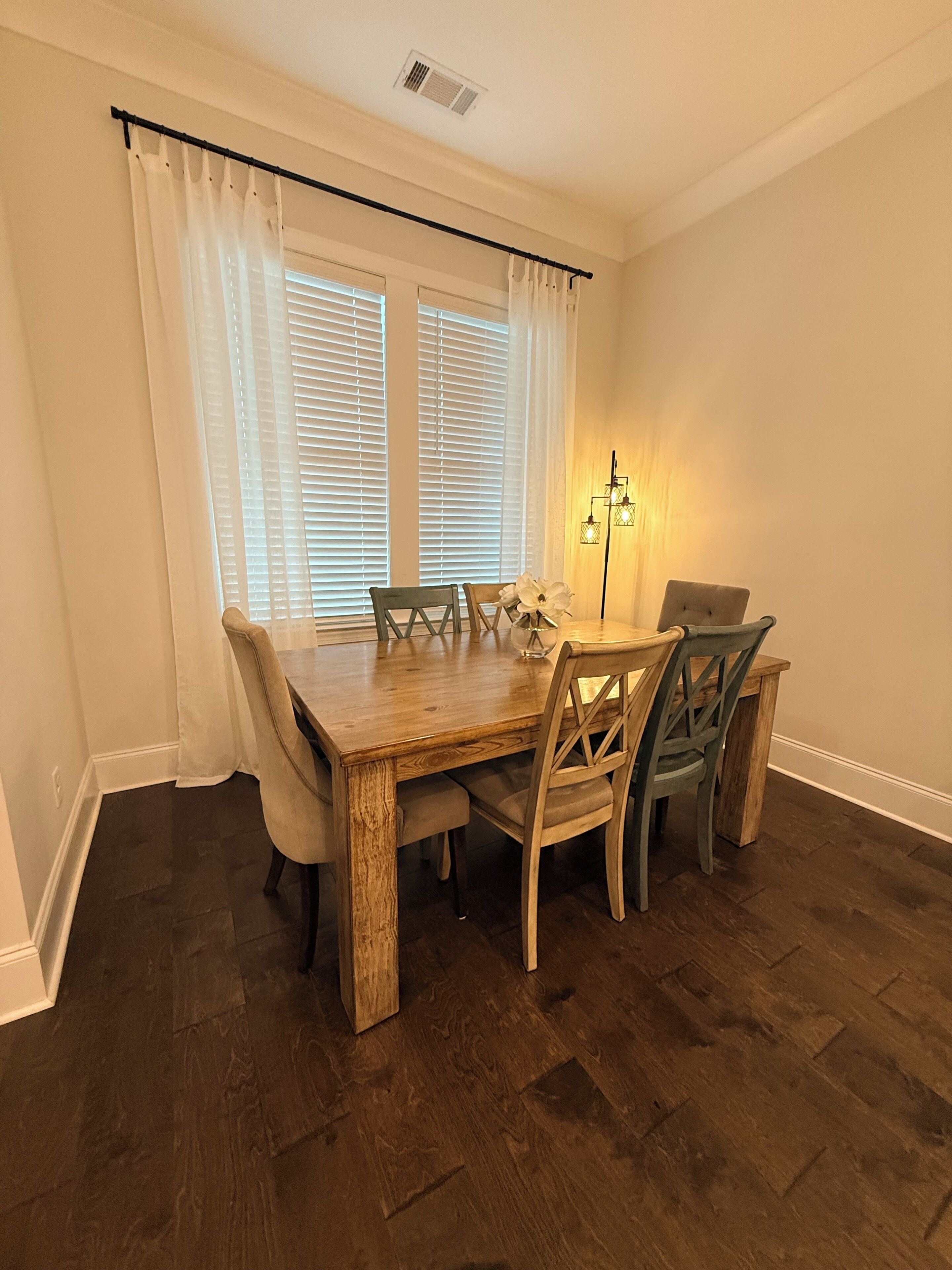 A dining area with a wooden table and chairs, a window with blinds, and a floor lamp.