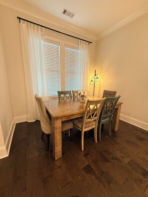 Un coin repas avec une table et des chaises en bois, une fenêtre avec des stores et un lampadaire.