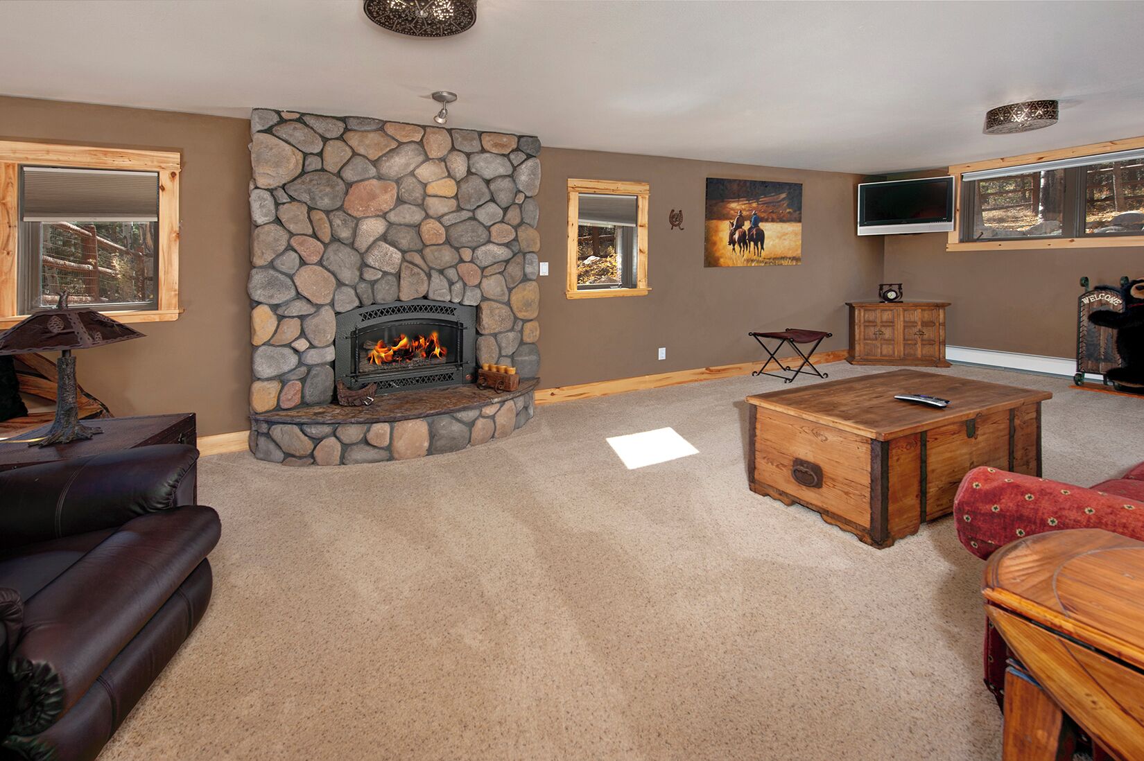 A cozy living room with a stone fireplace, leather furniture, and a mounted TV.