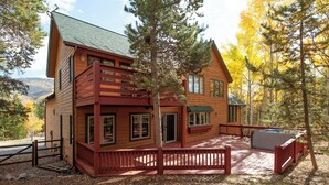 A wooden cabin with a deck and a hot tub, surrounded by trees and a mountain backdrop. - Mountain Home with Private Hot Tub (Silverthorne)