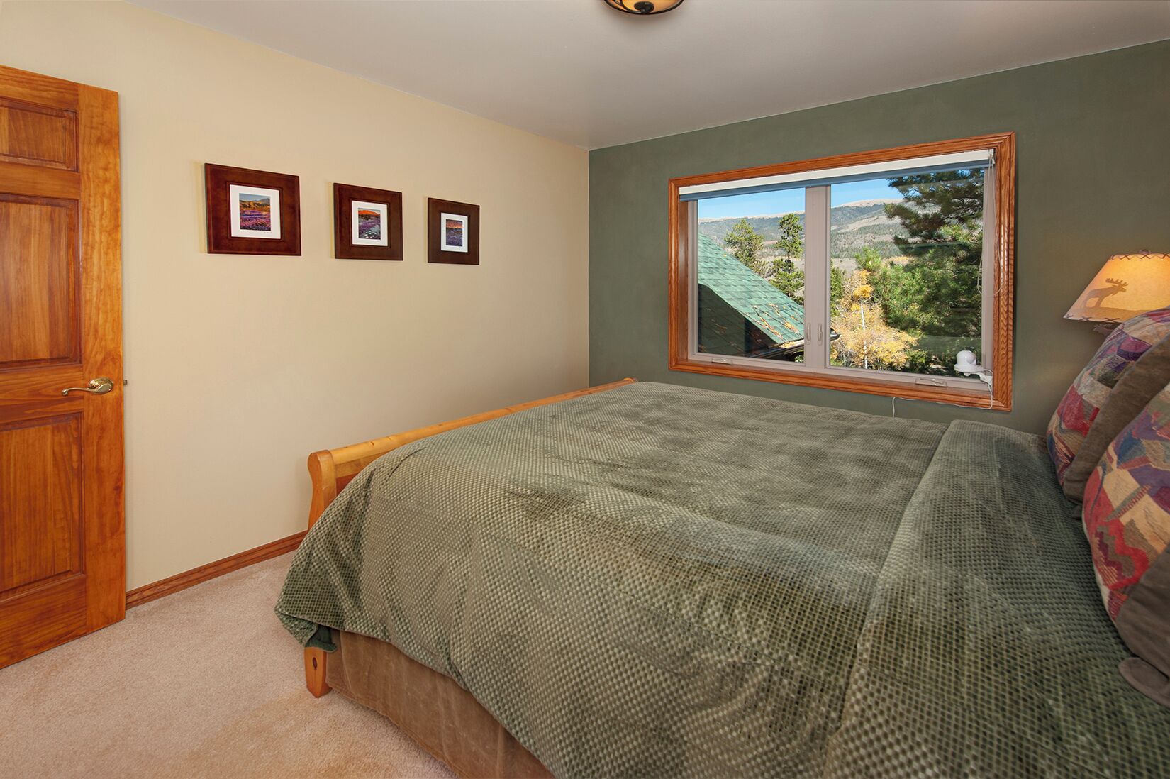 A bedroom with a bed, a window with a view of trees, and three framed pictures on the wall.