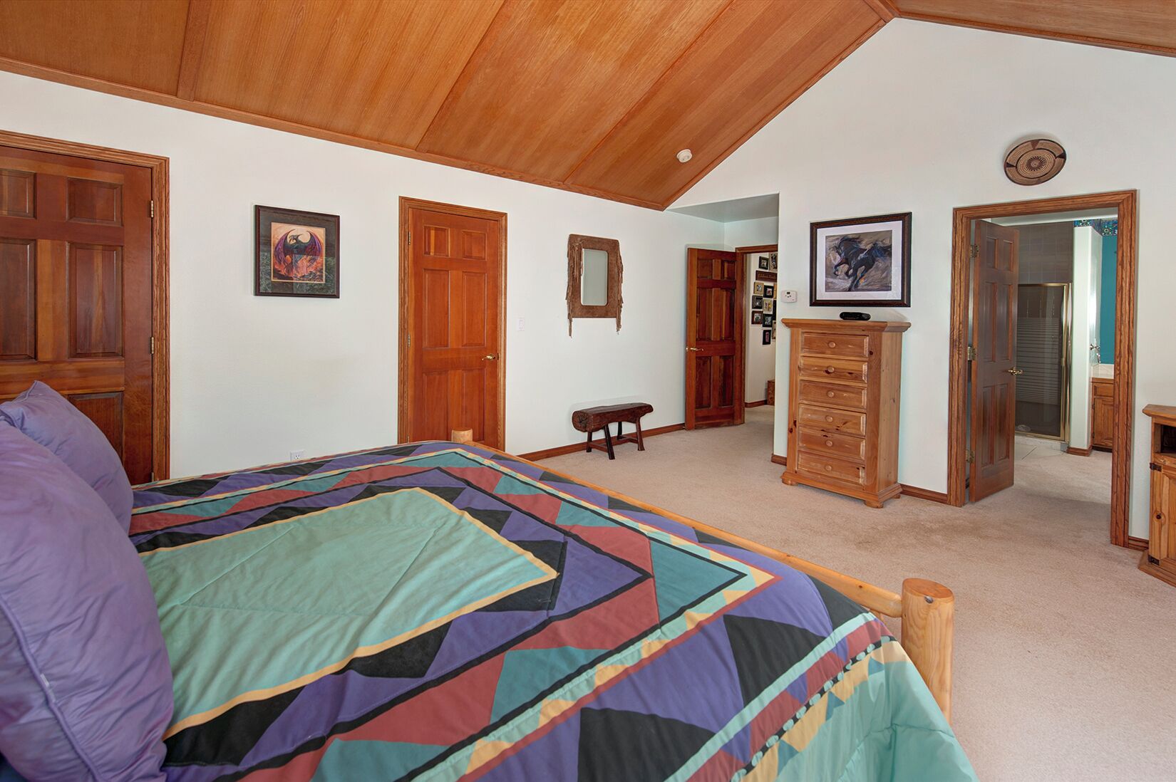 A bedroom with a large bed, wooden ceiling, and a dresser.
